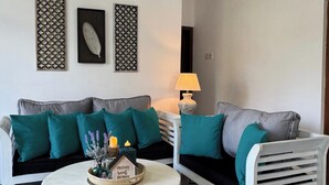 Una sala de estar con un sofá gris, cojines color turquesa, una mesa de centro redonda y dos paneles decorativos en la pared.