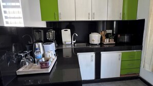 Una cocina moderna con encimeras negras, armarios blancos y verdes, un lavamanos, una estufa y un microondas.