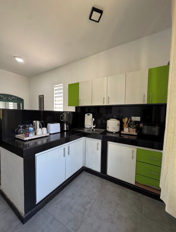 A modern kitchen with white and green cabinets, a black countertop, and various appliances including a coffee maker and toaster.