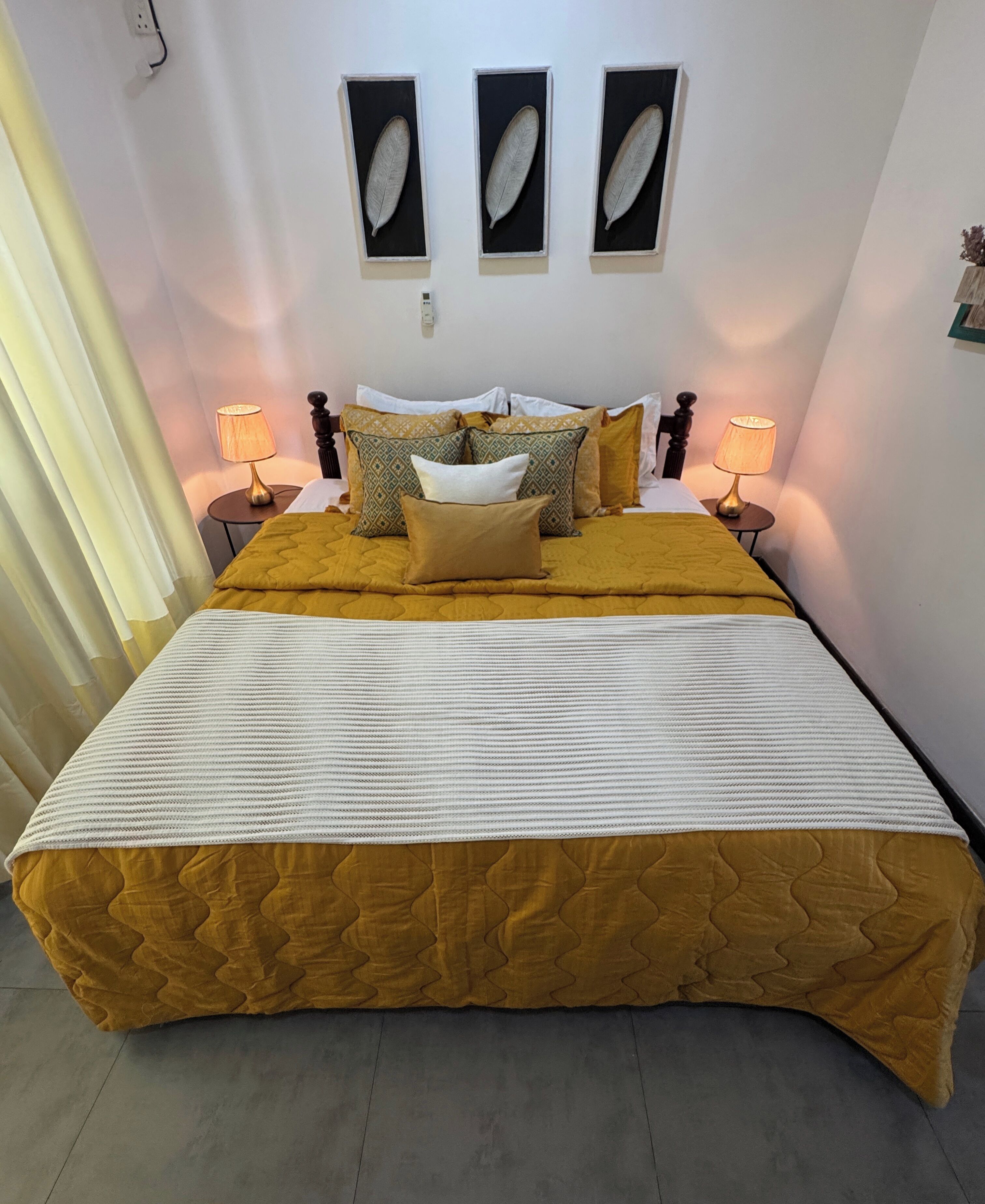 A bed with a yellow quilt, white pillows, and a white bedspread. There are two bedside tables with lamps.