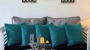 Una sala de estar con un sofá, cojines color turquesa, una mesita con un cartel decorativo de una casa y dos paneles en la pared con un patrón geométrico.