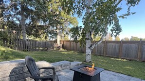 An outdoor patio with two black chairs and a square fire pit. - The Chieftain Suite (Barrie)