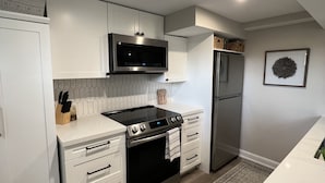 A modern kitchen with white cabinetry, stainless steel appliances, and a patterned rug. - The Chieftain Suite (Barrie)