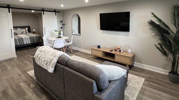 A modern living room with a grey sofa, a flat-screen TV mounted on the wall, and a wooden coffee table. - The Chieftain Suite (Barrie)