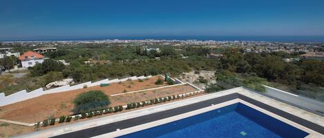 Una piscina rectangular con vistas despejadas del paisaje circundante, incluyendo una ciudad lejana y una masa de agua.