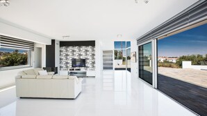 Een moderne woonkamer met een witte bank, een zwart-wit gestreept wandpaneel en een grote schuifglazen deur die leidt naar een terras.