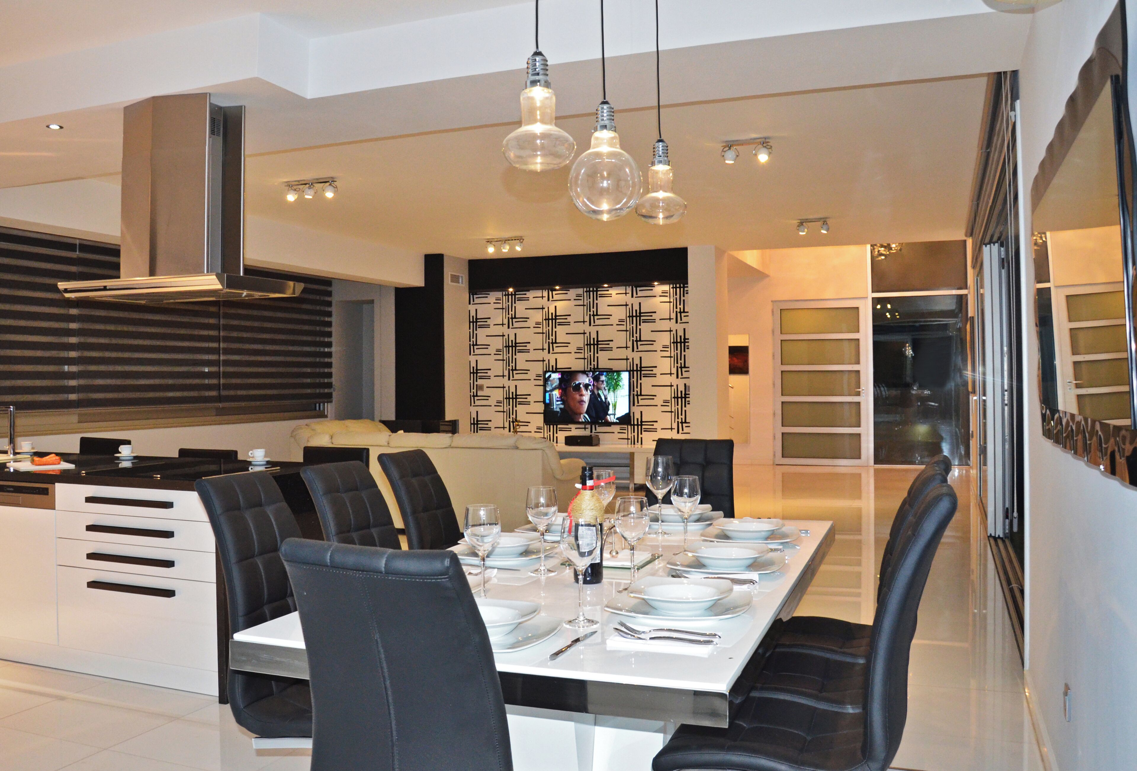A modern dining area with a long table set for six, black upholstered chairs, and pendant lighting.
