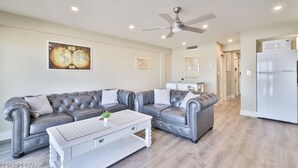 A modern living room with a grey leather sectional sofa, a white coffee table, and a ceiling fan. - Heart of Daytona 1 bedroom w/kitchen, sleeps 4, private balcony, fireplace, pool (Daytona Beach)