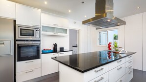A modern kitchen with built-in appliances, a large island, and a window providing natural light. - Villa Chloe (Vale do Lobo)