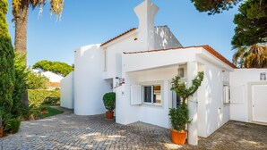 A white building with a red-tiled roof, a cobblestone driveway, and potted plants. - Villa Chloe (Vale do Lobo)