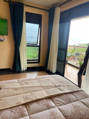 Ein Schlafzimmer mit Bett, einem Fenster mit Vorhängen und Blick auf eine grüne Landschaft.