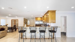 Una cocina moderna con armarios de madera, un refrigerador de acero inoxidable y una barra con cuatro sillas.