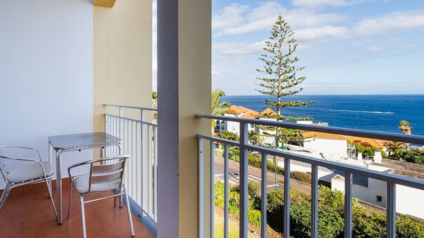 Un balcón con mesa y sillas, con vistas a la costa, edificios y un árbol.
