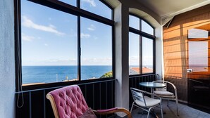 Un balcón con vista al mar, una silla acolchada, una mesita y otra silla.