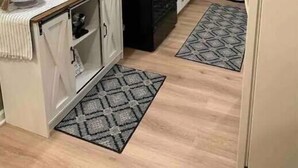 A kitchen with white cabinets, a black countertop, and a patterned rug. There are wall decorations and a small island with a sink. - The Landing Zone.
 Comfortable and cozy three bedroom with two car garage.  (East Moline)