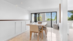 A modern dining area with a table and chairs, a basket, and a view of the outdoors through large windows.