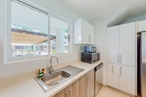Enjoy a kitchen with a large window, stainless steel sink, dishwasher, and white cabinetry.