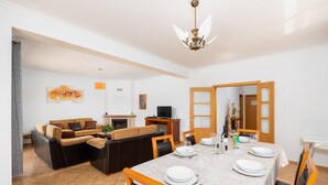 A dining area with a table set for four, a sofa set, a fireplace, and a television in the background.
