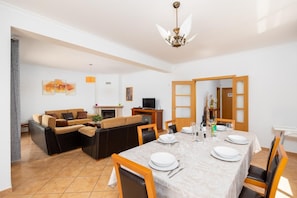 A dining area with a table set for four, a sofa set, a fireplace, and a television in the background.