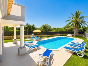 Una piscina con sillas reclinables azules y una palmera.