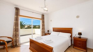 A hotel room with a bed, a chair, a nightstand, a lamp, and a view of the outside.
