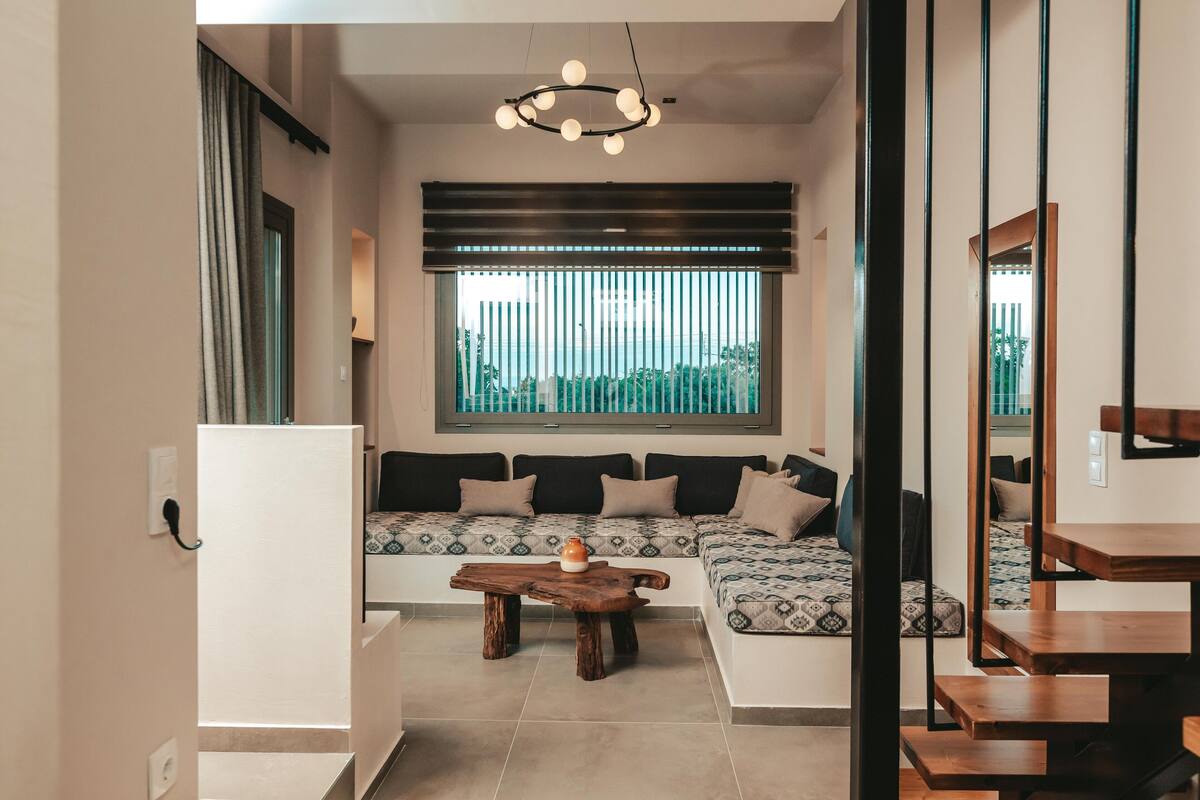 A modern living room with a sofa, a wooden coffee table, and a large window with blinds.