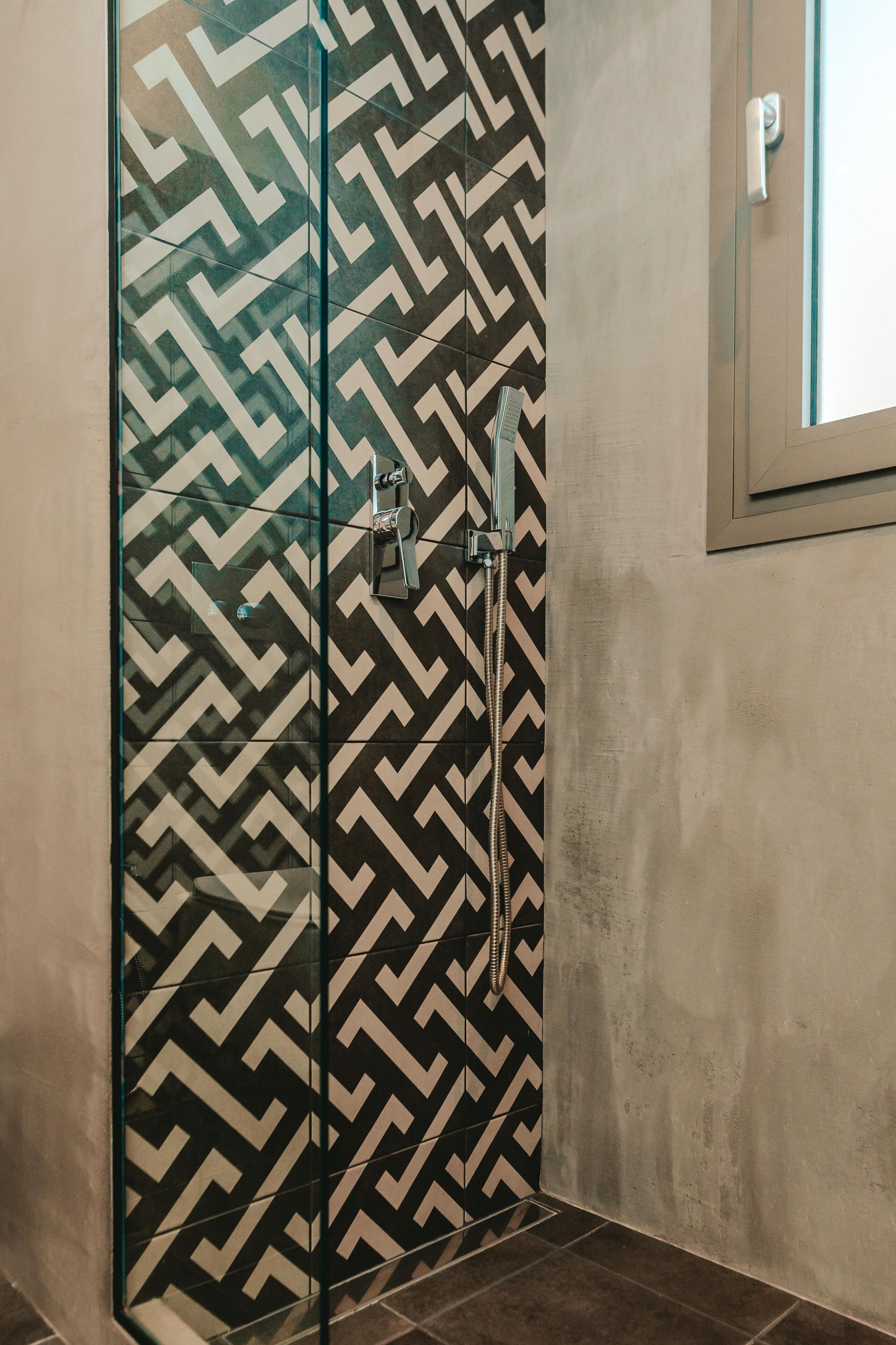 Ducha con un diseño de baldosas geométricas en la pared y puerta de vidrio.
