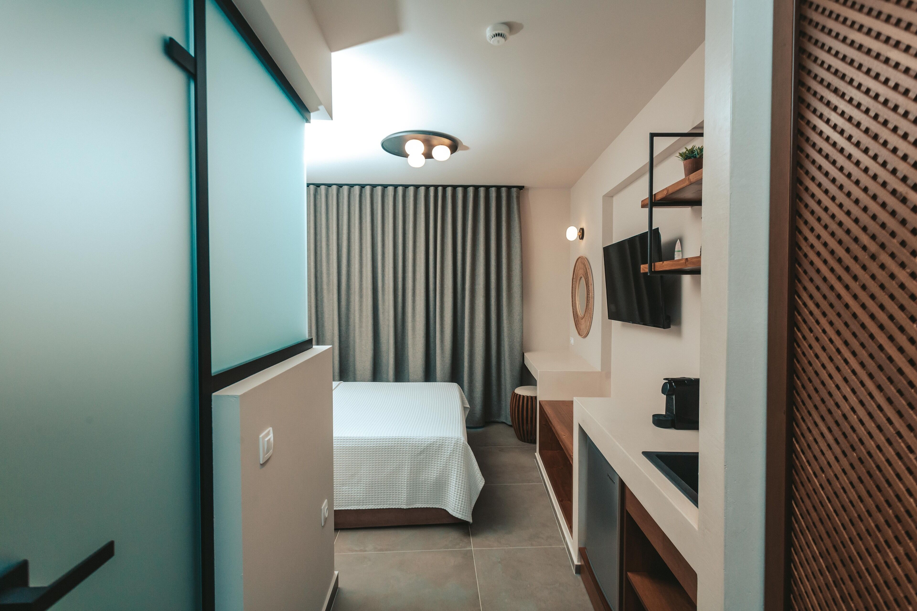 Una habitación de hotel moderna con cama, escritorio, televisor y ventana con cortinas.