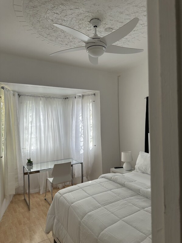 A bedroom with a bed, a desk, a chair, a lamp, and a ceiling fan.