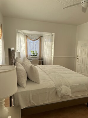 Une chambre à coucher avec un lit, une table de chevet, une lampe, une fenêtre avec des rideaux et une porte.