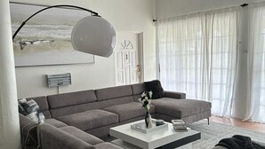 Un salon moderne avec un canapé d’angle, une table basse, un lampadaire et un ventilateur de plafond.