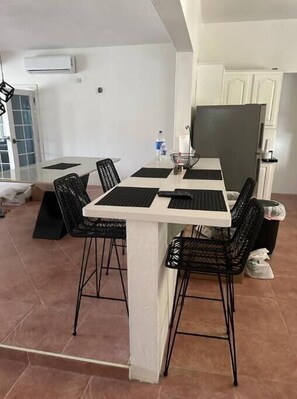 Un coin repas avec une table blanche et des chaises noires, une bouteille d’eau et un réfrigérateur.