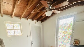 A room with a wooden ceiling, a ceiling fan, a window with a stained glass design, and a door.
