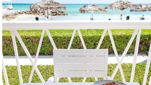 A table set with a variety of dishes, a glass of water, and cutlery, overlooking a beach with thatched umbrellas and a clear view of the ocean.