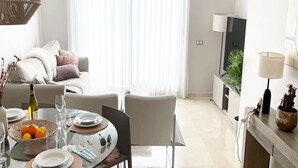 Una sala de estar moderna con comedor, un sofá, un televisor y una planta.