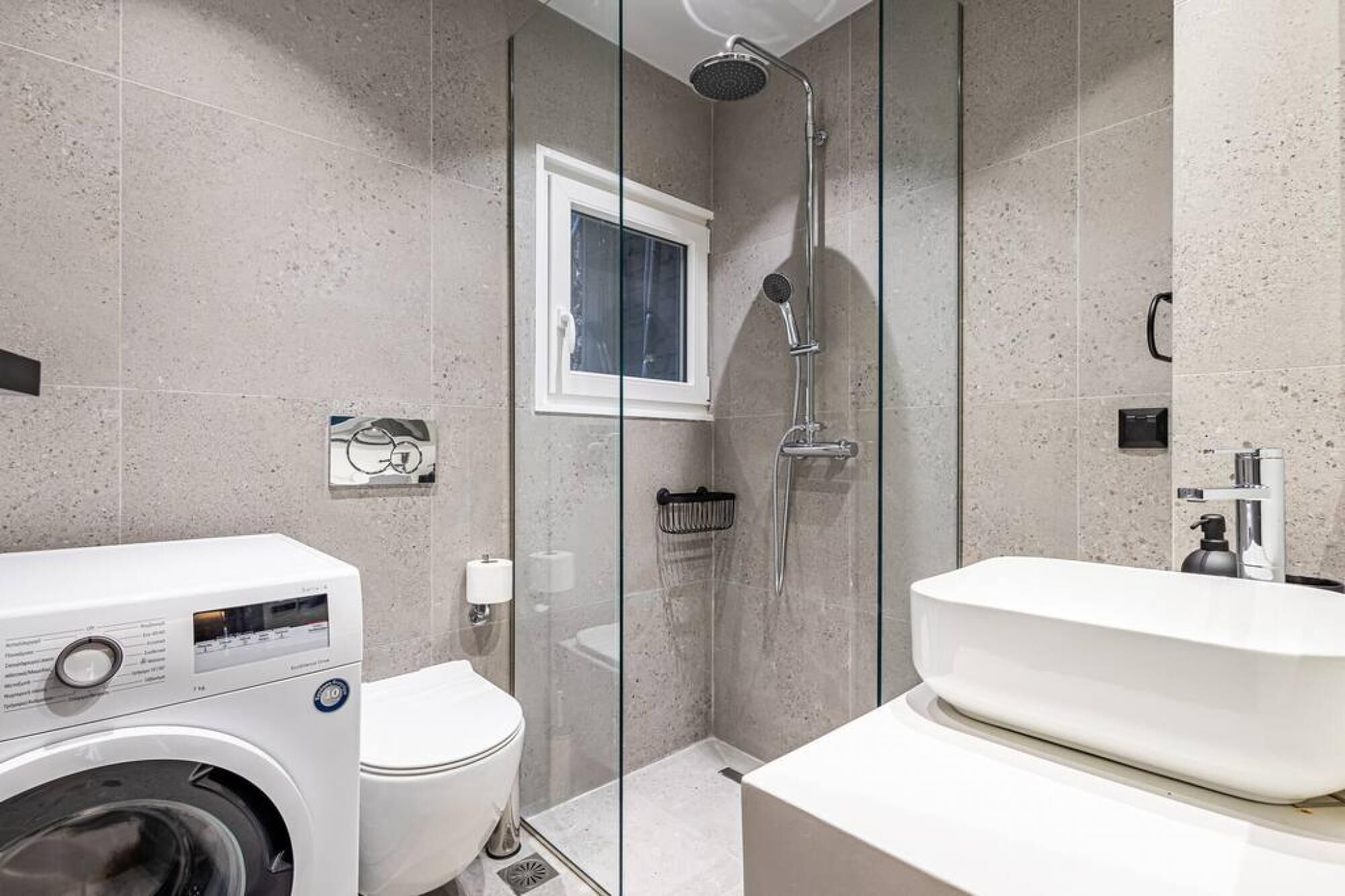 A modern bathroom with a glass-enclosed shower, a toilet, and a washing machine.