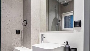 A modern bathroom with a large mirror, a white sink, and a shower area. - Philoxenia I Acropolis Museum (Athens)