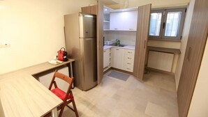 A compact kitchen with a built-in refrigerator, a dining table with a chair, and a window with blinds. - Elegant Studio at the Acropolis Hills (Athens)