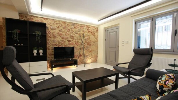 A modern living room with a stone wall, black furniture, a flat-screen TV, and a window with blinds. - Elegant Studio at the Acropolis Hills (Athens)