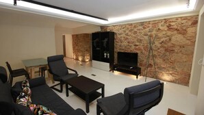 A modern living room with a sofa, chairs, a coffee table, a TV, and a stone wall. - Elegant Studio at the Acropolis Hills (Athens)