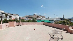 A rooftop terrace with a metal chair, a small trash bin, and a view of a historic building in the background. - Elegant Studio at the Acropolis Hills (Athens)
