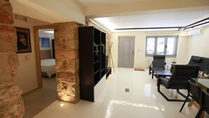 A modern living room with a stone column, a black entertainment unit, and a dining area with black chairs and a table. - Elegant Studio at the Acropolis Hills (Athens)