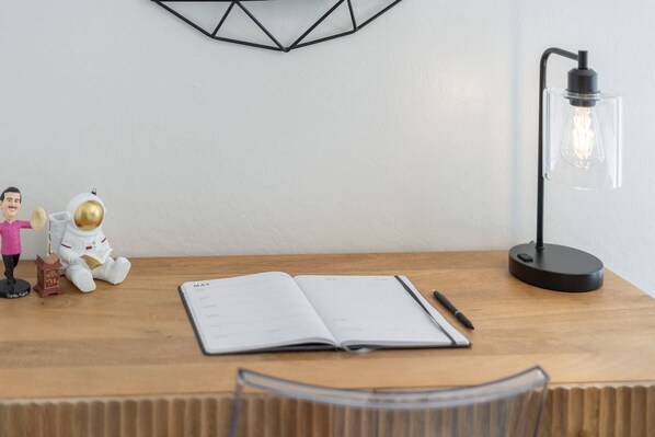 Une table en bois avec un carnet, un stylo, une lampe de bureau et deux figurines d’astronautes.
