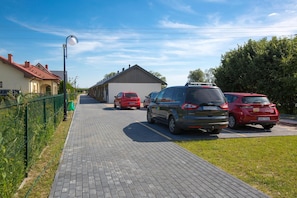 En asfalterad uppfart med parkerade bilar, en byggnad med ett sluttande tak och en klar himmel.