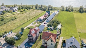 Vue aérienne d’un quartier résidentiel avec des maisons, une longue rangée de voitures garées et une étendue d’eau en arrière-plan.