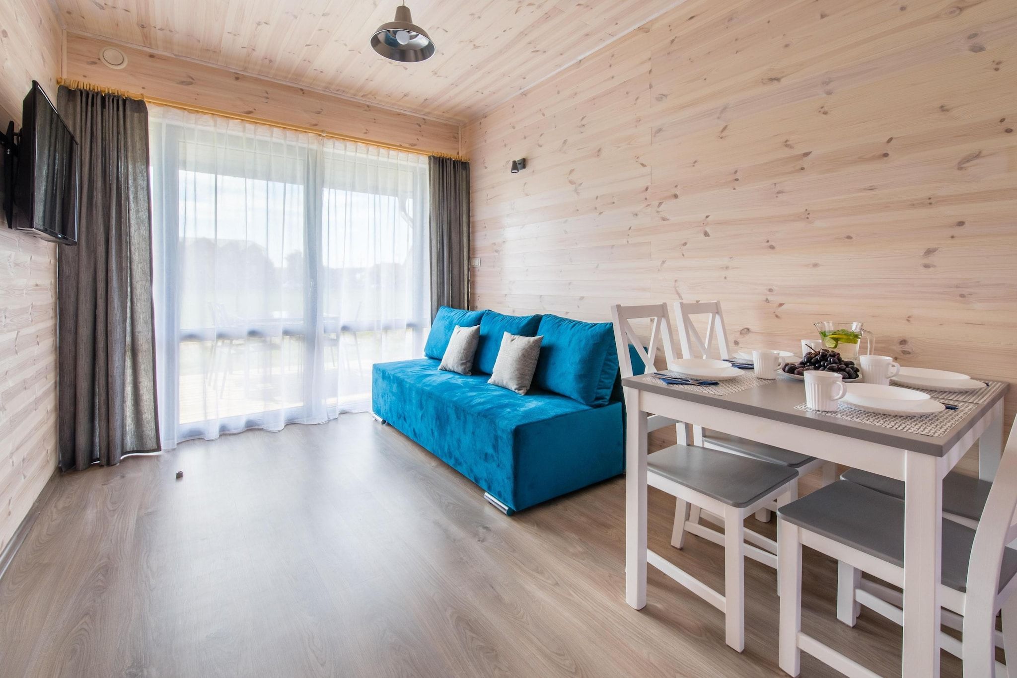 A modern room with a blue sofa, a dining table with chairs, and a large window with curtains.