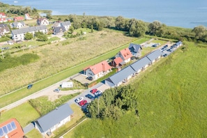Ett flygbildsbild av ett bostadsområde med hus, en parkeringsplats och en vattenyta i bakgrunden.