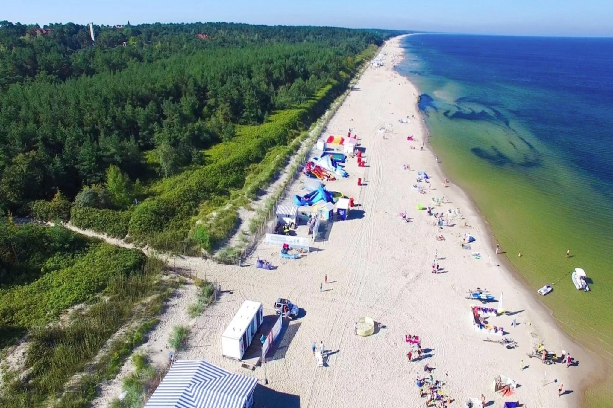 Een strand met een rij strandhutten en parasols, een helder uitzicht op de oceaan, en een bebost gebied op de achtergrond.
