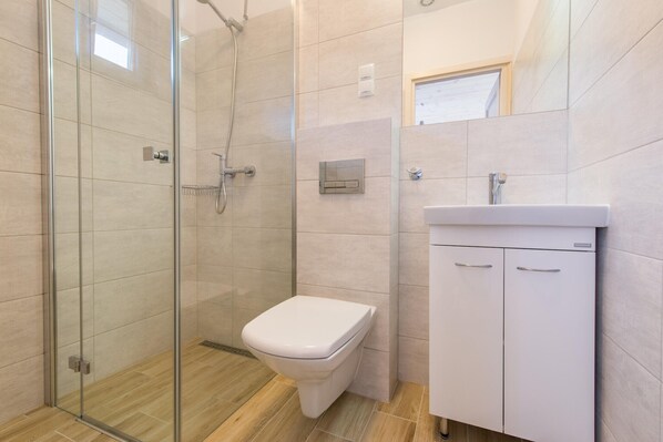 A modern bathroom with a glass shower enclosure, a white toilet, and a white sink with a cabinet.