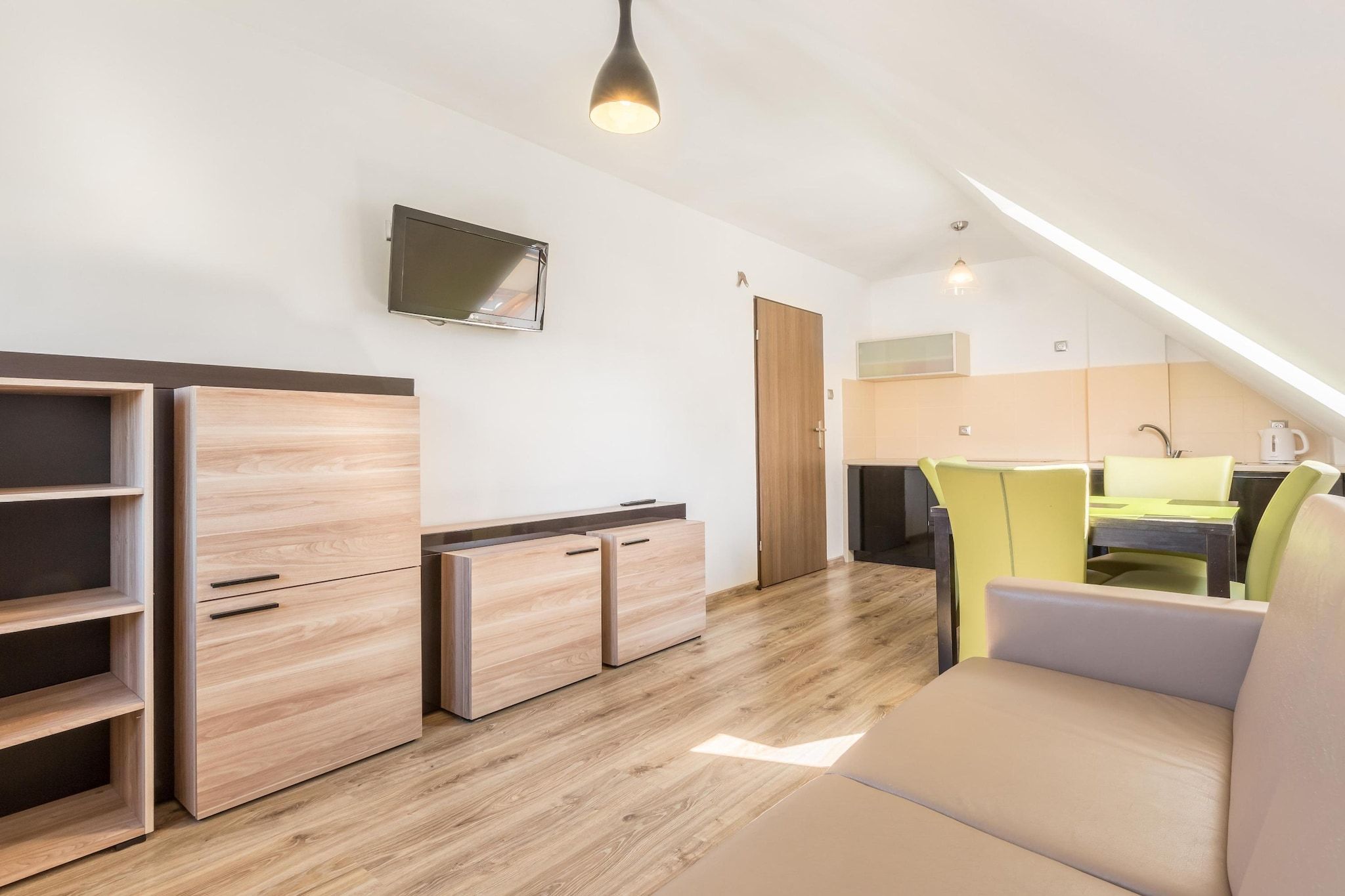 Habitació moderna i ben il·luminada amb terres de fusta, un sofà, una taula de dinar amb cadires i una zona de cuina.